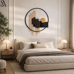 May include: A circular wall art piece featuring a black metal frame, vertical gold rods, black rectangular panels, and a solid gold circle. The artwork is mounted on a white wall above a beige upholstered bed with pillows and a brown throw.
