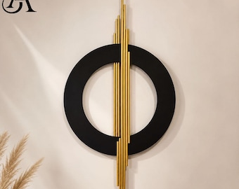 May include: A wall art piece featuring a large matte black circular frame intersected by a vertical arrangement of slender gold-toned metal rods of varying lengths. The design includes a logo in the top left corner with the letters SA.