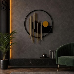 May include: A circular wall art piece featuring a black metal frame, vertical gold-toned rods of varying lengths, a solid black rectangular panel, and a single gold-toned circular disc positioned on the right side of the composition.