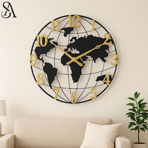 Op de afbeelding: Een zwarte en gouden wereldkaart wandklok. De klok heeft een zwart wereldkaart silhouet met goudkleurige cijfers en wijzers. De klok is rond en heeft een rasterpatroon. De klok hangt aan een crèmekleurige muur.
