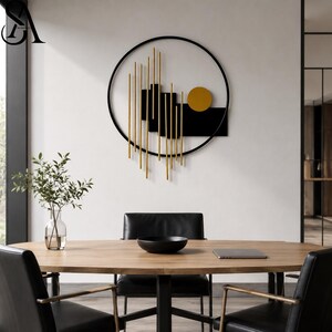 May include: A circular wall art piece featuring a black metal frame, vertical gold rods of varying lengths, black rectangular panels, and a solid gold circle. The design is abstract and geometric, mounted on a plain white wall surface.