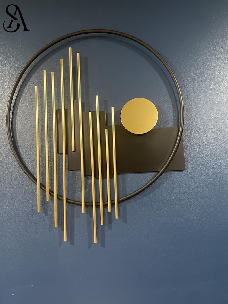 May include: A circular black metal wall art piece featuring a series of vertical gold-toned rods of varying lengths arranged in a linear pattern, accompanied by a solid black rectangular plate and a single gold-toned circular disc element.