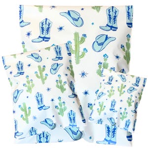 Könnte beinhalten: Weiße Verpackung mit einem sich wiederholenden Muster aus blauen Cowboy-Stiefeln, Hüten, Kakteen und Sternen. Die Verpackung ist in drei verschiedenen Größen erhältlich, wobei die größte im Hintergrund und zwei kleinere im Vordergrund sind.