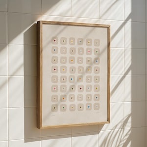 May include: A framed abstract art print featuring a grid of beige squares, each containing a small, colorful dot. The dots are in various colors, including red, blue, yellow, and green. The frame is made of light-colored wood.