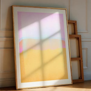 Puede incluir: Una gran impresión artística abstracta enmarcada con un marco dorado. La obra de arte presenta un degradado de colores, incluyendo amarillo, rosa y azul. La impresión está apoyada contra una pared, con un marco de madera en el fondo. La obra se exhibe sobre un suelo de madera.