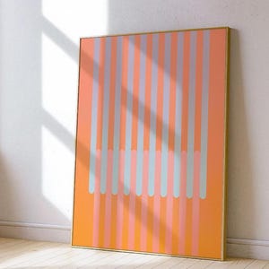May include: Abstract art print with vertical stripes in orange, pink, and blue. The artwork is framed in a gold-coloured frame and leans against a white wall. The design is modern and minimalist, suitable for various interiors.