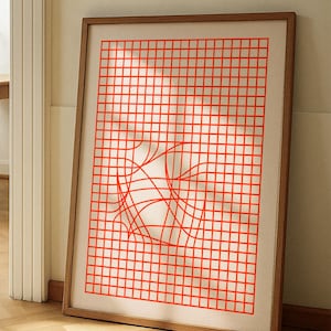 May include: A framed art print featuring a red grid pattern with a distorted central design. The artwork is displayed in a wooden frame, adding a touch of warmth to the modern aesthetic. The print is displayed against a neutral background.