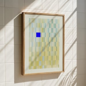 Könnte beinhalten: Abstrakter Kunstdruck in einem Holzrahmen. Das Kunstwerk zeigt ein Raster aus vertikalen Rechtecken in Gelb-, Grün- und Blautönen mit einem durchgehenden blauen Quadrat in der Nähe der Mitte. Die gerahmte Kunst ist an einer weiß gefliesten Wand befestigt.