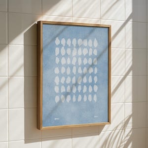 May include: A framed art print featuring a light blue background with a pattern of white, irregular shapes. The artwork is enclosed in a natural wood frame and mounted on a white tiled wall. The print has the text "-" and "MEET" in the bottom corners.