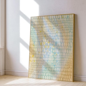 May include: Abstract art print in a gold frame. The artwork features a pattern of white, yellow, and blue shapes on a light yellow and blue background. The framed art is leaning against a white wall, with natural light and shadows.