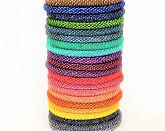 May include: A stack of fifteen flexible beaded bracelets in a spectrum of colours including bronze, blue, green, teal, purple, red, coral, orange, yellow, and grey. Each bracelet is constructed from small, uniform glass beads.