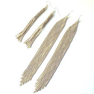 May include: Four pairs of silver beaded earrings. Two pairs are long, with multiple strands of beads, and two pairs are shorter, with a twisted design. All have silver hooks.
