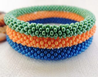 May include: Three beaded bracelets stacked on top of each other. The top bracelet is green, the middle bracelet is orange, and the bottom bracelet is blue.