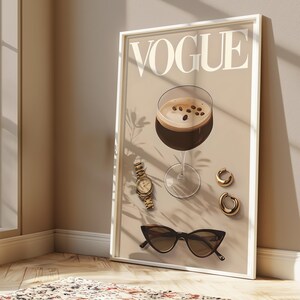 Puede incluir: Una portada de la revista Vogue con una bebida de caf&eacute; marr&oacute;n en un vaso, un reloj dorado y pendientes de aro dorados sobre un fondo beige.