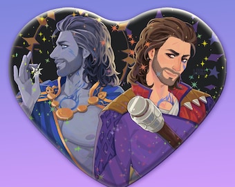 May include: A heart-shaped pin featuring a digital illustration of two figures with long brown hair and facial hair. One figure has blue skin and wears a blue garment with a gold necklace, while the other wears a purple and red outfit with a staff.