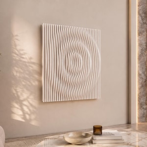 May include: A white, textured wall art piece with a wave-like design. The artwork is mounted on a beige wall in a modern living space. The room features a sofa, a potted plant, and a marble coffee table.