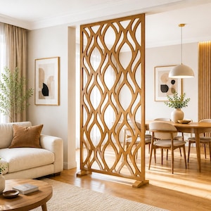 Op de afbeelding: Een hoge, rechthoekige houten ruimteverdeler met een herhalend, opengewerkt golfpatroon. De structuur is gemaakt van lichtgekleurd hout en staat op twee rechthoekige voeten, wat een halfdoorzichtige scheidingswand tussen twee ruimtes vormt.