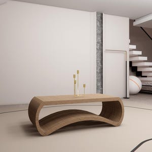 May include: A modern, curved wooden coffee table with a layered design. The table is light brown and has a unique, open-bottom design. Gold candle holders with three candles are on top. The room has a neutral color palette.