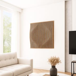 Puede incluir: Una obra de arte mural de madera con un diseño de listones verticales ondulados. La obra de arte está enmarcada en madera de color marrón claro y montada en una pared blanca. La habitación también cuenta con un sofá blanco, una mesa de centro redonda de mármol y un jarrón negro.