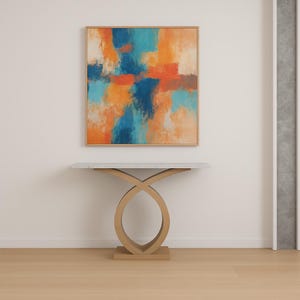 以下が含まれることがあります： 木製のフレームに入った抽象画。オレンジ、青、ターコイズの筆致が特徴です。その下に、大理石の天板と、交差するループデザインの明るい木製のベースを備えたモダンなコンソールテーブルがあります。