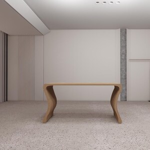 May include: A light-colored wooden desk with a unique, curved leg design. The desk has a long, rectangular top and is set against a neutral-toned wall. The room has a terrazzo floor.