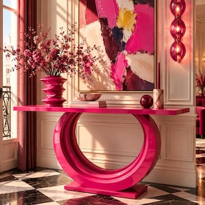May include: A bright magenta console table with a circular base, topped with a matching magenta vase containing pink blossoms, a small bowl on books, a dark red sphere, and a tall candle in a marble holder, set against a large abstract painting.