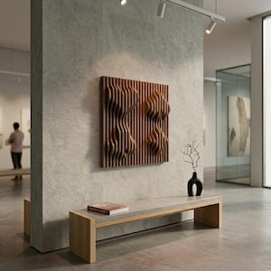 May include: A wooden wall art piece with a relief design of two abstract figures. The artwork is made of vertical wooden slats, creating a textured, three-dimensional effect. The piece is mounted on a gray concrete wall in a gallery setting.