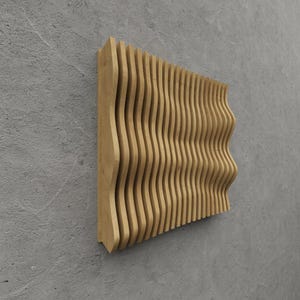 Op de afbeelding: Een houten wandkunstwerk met een golfachtig ontwerp. De kunst is gemaakt van verticale, gebogen houten latten, waardoor een gestructureerd, driedimensionaal effect ontstaat. Het hout heeft een natuurlijke, lichtbruine kleur. Het stuk is op een grijze muur gemonteerd.