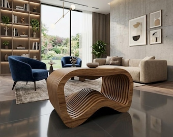 May include: A modern living room featuring a unique wooden coffee table with a wave-like design. The room includes blue armchairs, a beige sofa, and a large window overlooking a garden. The floor is a dark, glossy material.