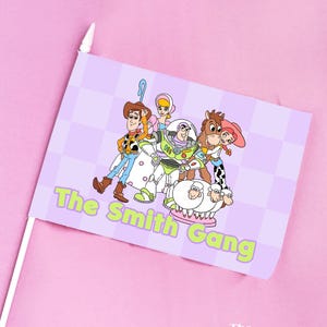 May include: A small flag featuring a cartoon image of characters from the Toy Story franchise. The flag has a light purple checkered background and the text "The Smith Gang" in green. The flag is on a white stick.