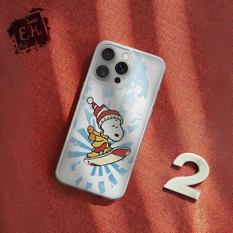 May include: Clear phone case featuring a cartoon Snoopy character wearing a Santa hat and surfing on a red and white surfboard. The design includes a blue and white sunburst background. The case is on a red-orange textured surface.