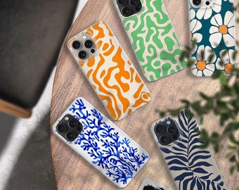 May include: A collection of smartphone cases with various designs. The cases feature patterns such as orange abstract shapes, green squiggles, white daisies on teal, blue coral, and navy zebra stripes. The cases are displayed on a light brown surface.