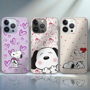 Könnte beinhalten: Drei Handyhüllen mit Snoopy-Designs. Die erste ist helllila mit dunkelvioletten Herzen und Snoopy, der Blumen hält. Die zweite hat Snoopy mit einem roten Herzmuster. Die dritte ist beige mit Snoopy und Herzen.