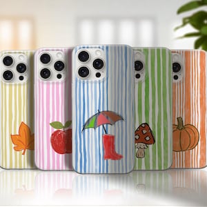 Op de afbeelding: Vijf smartphonehoesjes op een rij, elk voorzien van verticale, handgetekende strepen en een uniek icoon: een oranje blad, een rode appel, een kleurrijke paraplu met een rode regenlaars, een bruine paddenstoel en een oranje pompoen.