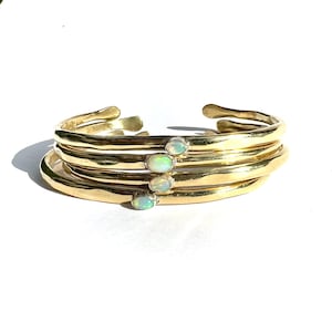 May include: A gold bracelet with four bands and three opal stones. The bracelet is made of hammered metal and has a rustic look.