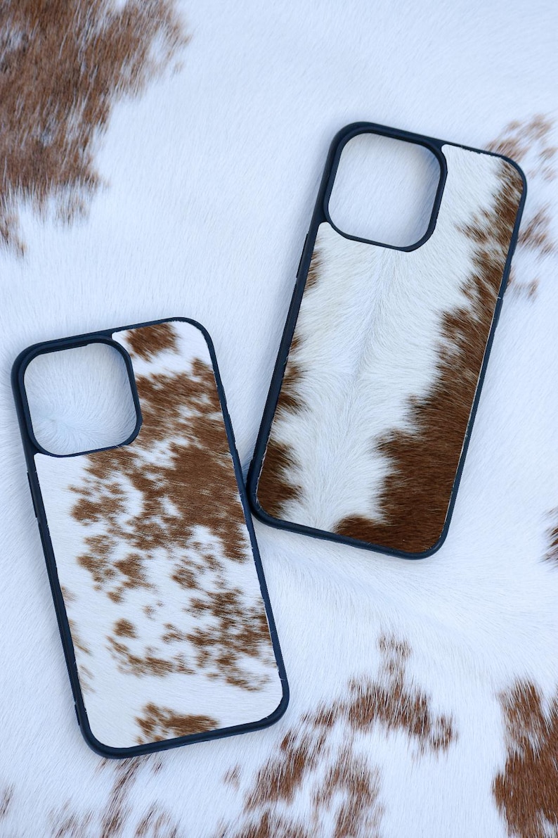 Pu&ograve; includere: Due custodie per telefono con un design in pelle di mucca. Le custodie hanno un bordo nero e un motivo maculato bianco e marrone. Le custodie sono esposte su uno sfondo di pelle di mucca bianca e marrone.