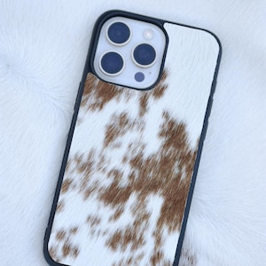 Pu&ograve; includere: Custodia per telefono con bordi neri e motivo a pelle di mucca. La custodia presenta uno sfondo bianco con macchie marroni e un modulo fotocamera con tre lenti. La custodia &egrave; progettata per proteggere il telefono.