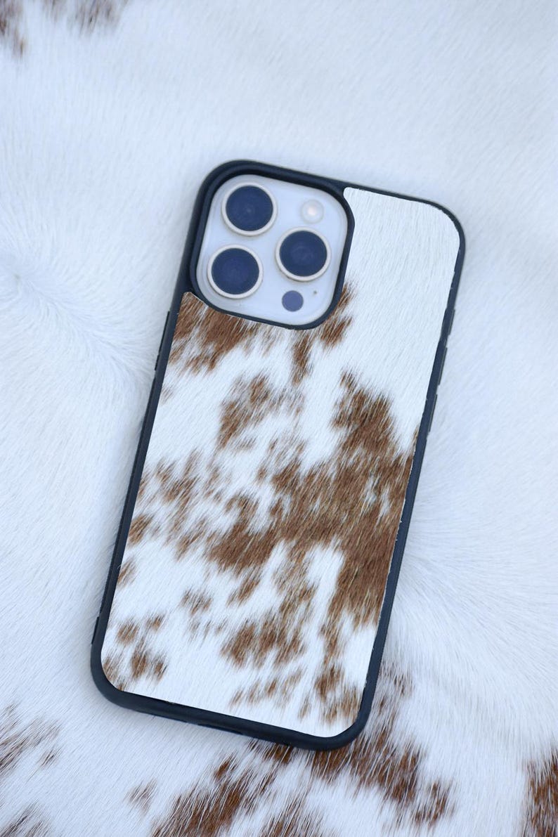 Pu&ograve; includere: Custodia per telefono con bordi neri e motivo a pelle di mucca. La custodia presenta uno sfondo bianco con macchie marroni e un modulo fotocamera con tre lenti. La custodia &egrave; progettata per proteggere il telefono.