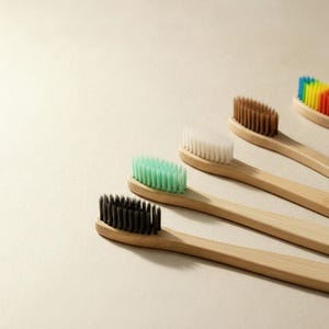 May include: Five bamboo toothbrushes with different colored bristles: black, green, white, brown, and rainbow. The toothbrushes are arranged diagonally, showcasing their natural wood handles and colorful bristles. Eco-friendly dental hygiene products.