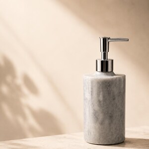 May include: A cylindrical soap dispenser crafted from grey and white marbled stone. The dispenser features a polished chrome pump mechanism at the top, designed for dispensing liquid soap or lotion with a simple downward press of the nozzle.
