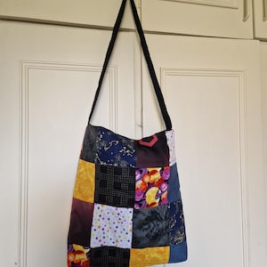 May include: A patchwork tote bag with a black strap. The bag is made of various fabric squares in colours like yellow, blue, purple, and black. Some squares feature celestial and space-themed patterns, including stars and planets.