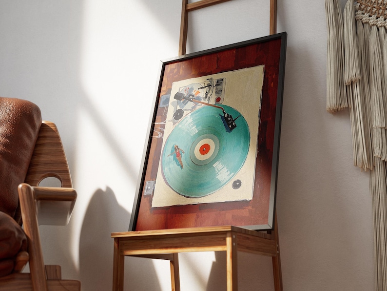 May include: A framed artwork featuring a vintage turntable design. The artwork has a teal record with a red center, set against a cream background. The frame is black, and the artwork is displayed on a wooden stand.