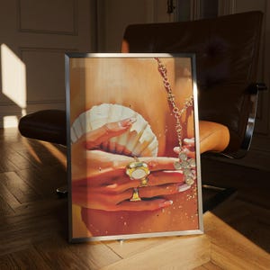 May include: A framed artwork featuring a close-up of hands holding a seashell and wearing gold rings. A gold necklace with a cross pendant is also visible. The artwork has a warm color palette with gold and orange tones.