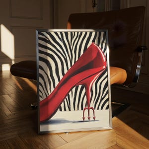 Puede incluir: Obra de arte enmarcada que presenta un zapato de tacón rojo vibrante con un tacón de tridente diabólico. El fondo muestra un patrón de rayas de cebra en blanco y negro. La obra está enmarcada en un marco plateado.