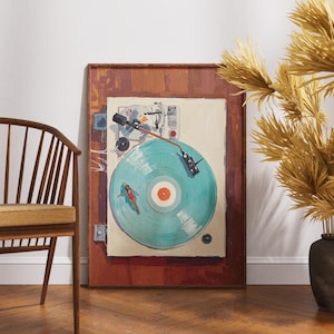 May include: A framed artwork depicts a vintage record player with a turquoise vinyl record. The artwork is set against a white wall, with a wooden chair and decorative dried plants in the foreground. The frame is a dark brown color.