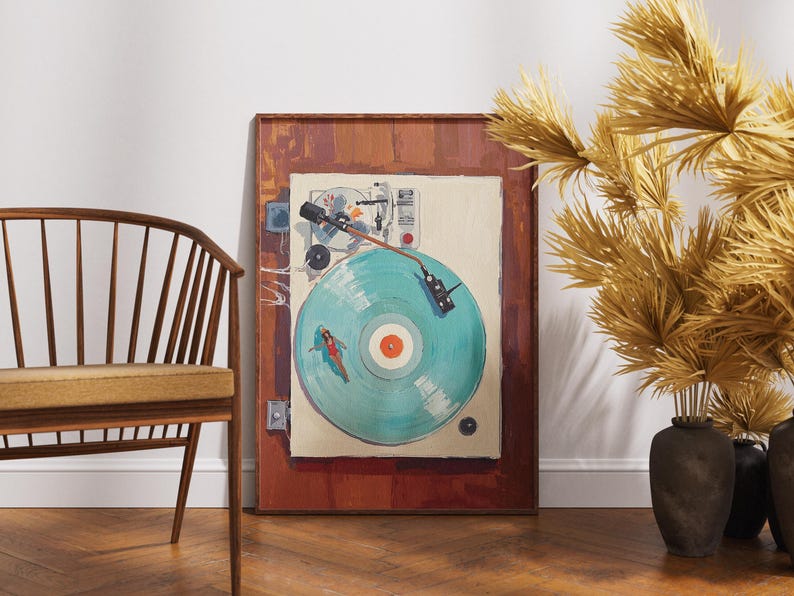 May include: A framed artwork depicts a vintage record player with a turquoise vinyl record. The artwork is set against a white wall, with a wooden chair and decorative dried plants in the foreground. The frame is a dark brown color.