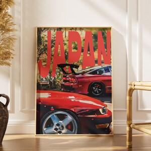 May include: A framed poster with the word "JAPAN" in large red letters. The poster features two red sports cars. The cars are partially visible, showcasing their sleek design and wheels. The background suggests a scenic outdoor setting.