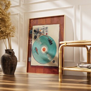 May include: A framed artwork featuring a vintage record player with a teal vinyl record. The artwork has a brown frame and is leaning against a white wall. A decorative vase with dried plants and a bamboo side table are also in the image.