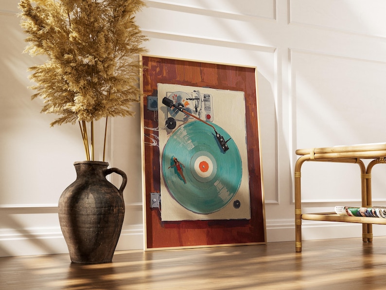 May include: A framed art print of a vintage record player with a teal record. The artwork has a warm color palette with a red-brown border and a light beige background. A dark brown vase with dried plants is to the left.