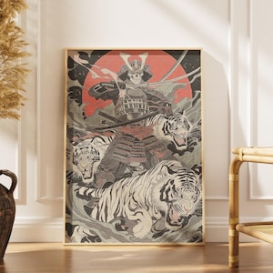 Op de afbeelding: Ingelijste kunstprint met een samoerai-krijger met een schedelgezicht, gehuld in een harnas, omringd door drie tijgers. Het kunstwerk is in tinten rood, grijs en zwart, met een rode zon op de achtergrond. De lijst is goudkleurig.
